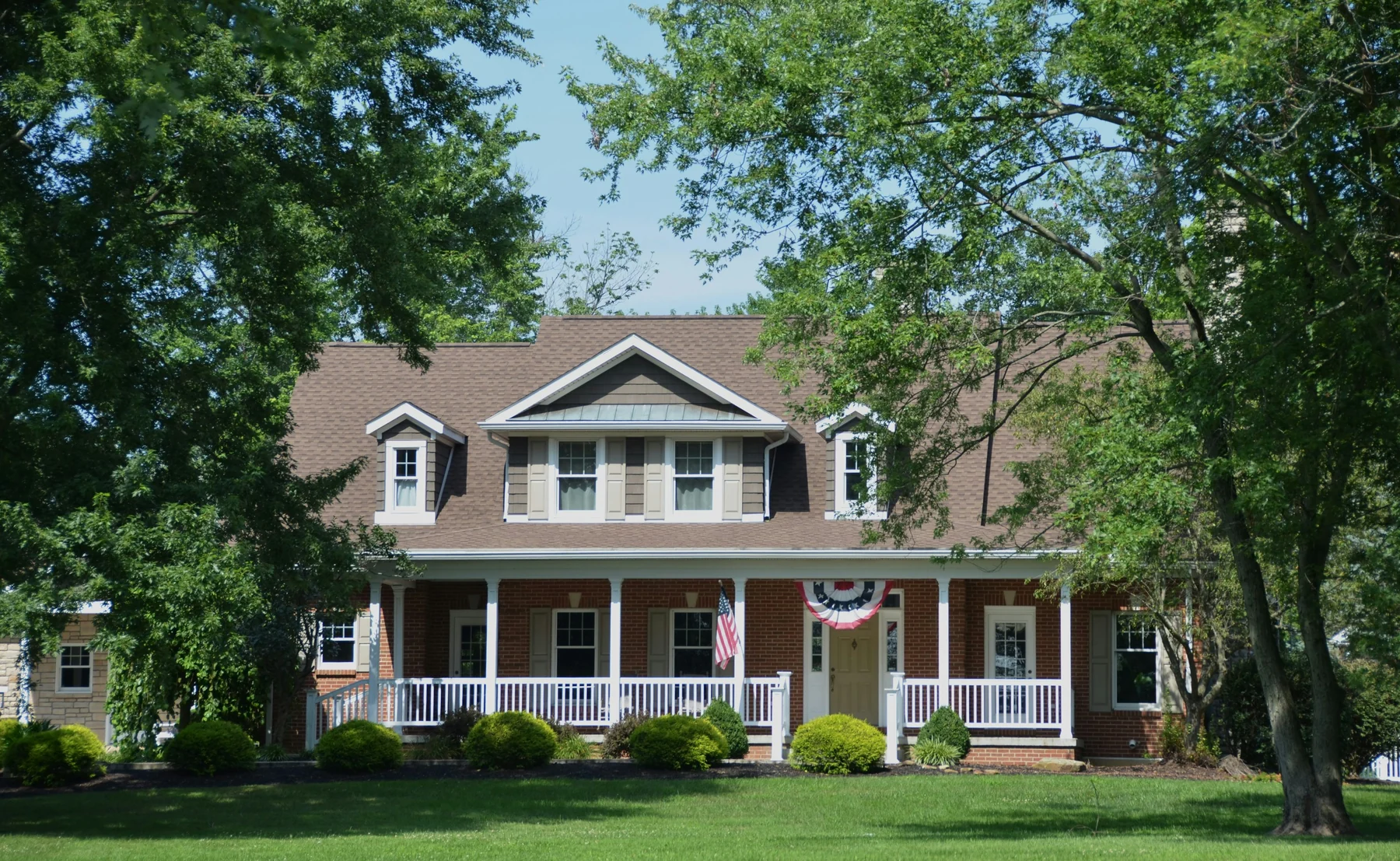 Traditional brick home with a deep front porch, mature shade trees and landscaped grounds; illustrative Southern architecture, not a Watchman project